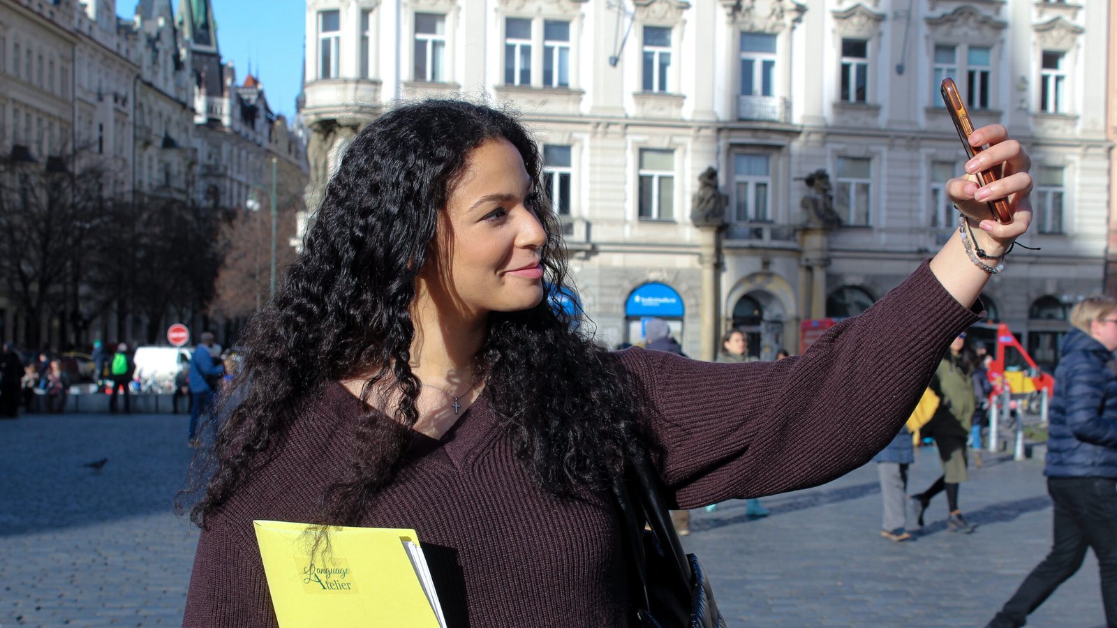 Woman taking a selfie with Language Atelier notebook in city square